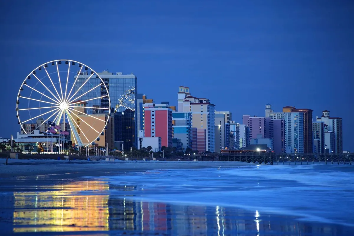 A vibrant exterior scene featuring a ferris wheel, colorful buildings, and the shimmering ocean at sunset. The lively ambiance captures the excitement of nearby attractions and the unique coastal nightlife, hinting at experiences beyond the resort.