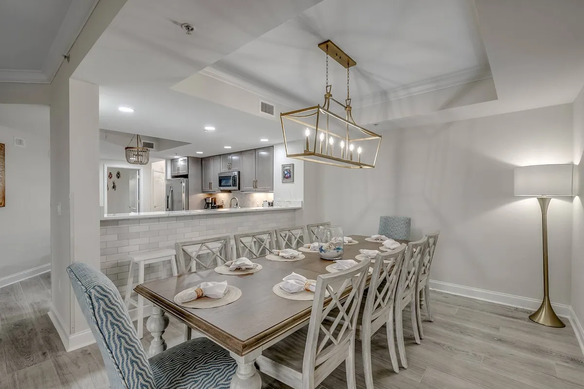 A warm dining area with a large dining table, beautiful lighting fixture, and clear visibility of the adjacent kitchen. The space feels inviting and is set up for family dinners or celebratory gatherings, with a welcoming ambiance and room for multiple guests.