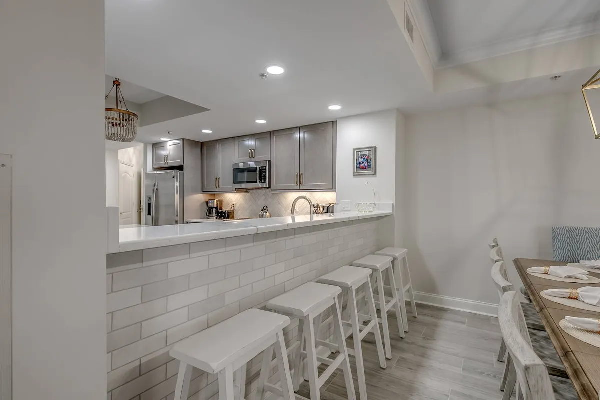 This image features a kitchen island, bar stools, a dining table, and sleek cabinetry. The kitchen area is modern and spacious, with ample room for preparing meals, entertaining, and casual dining. The bar stools at the island invite conversation and social interaction while cooking.
