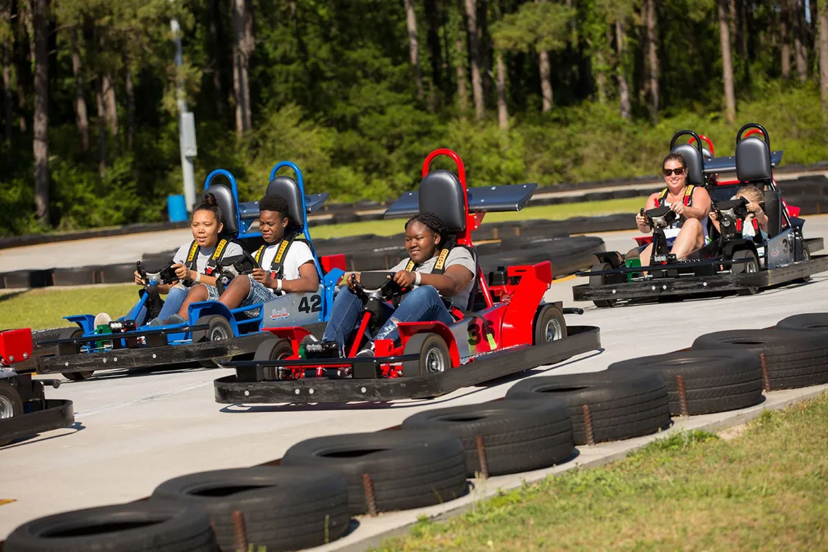An outdoor racetrack bustling with go-karts in action, participants of all ages enjoying friendly competition, and bright safety barriers outlining the course. The mood is energetic and joyful, perfect for group adventures.