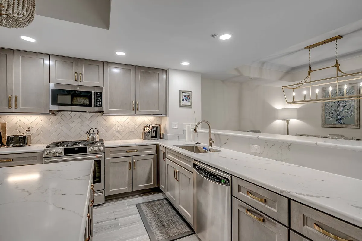 A stylish kitchen with marble countertops, stainless steel appliances, a herringbone backsplash, and gold hardware. The space looks sophisticated and ready for serious cooking, featuring all the amenities a chef might need for preparing anything from coffee to elaborate meals.