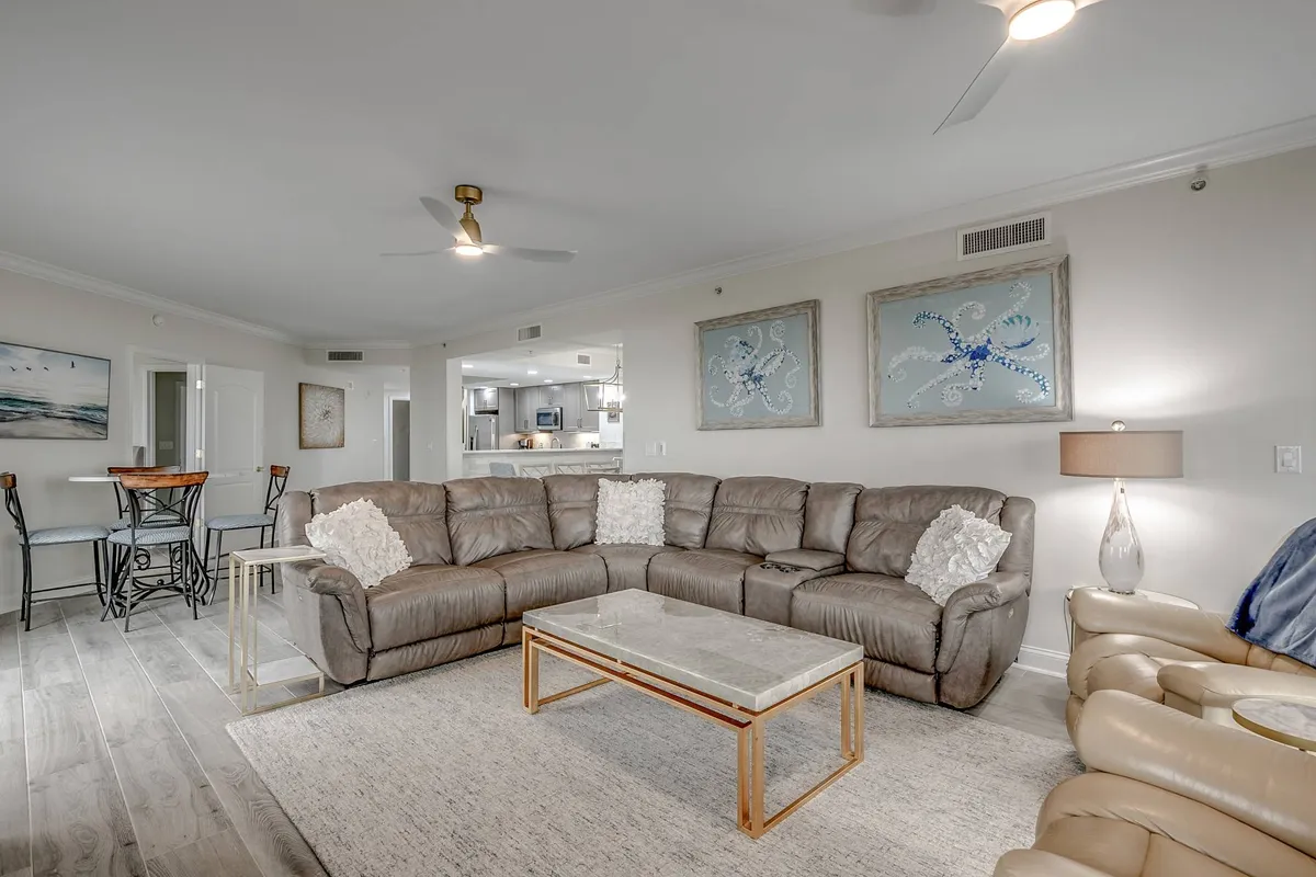 An inviting open living area featuring a large sectional sofa, coffee table, stylish wall art, and a view of the dining area beyond. The setup is perfect for both intimate conversations and larger gatherings, with a warm, welcoming atmosphere.