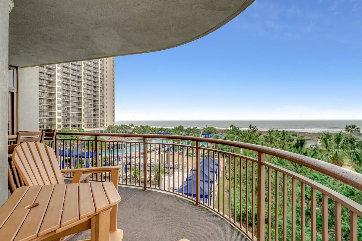A serene balcony scene with comfortable seating, lush tropical vegetation, and an unobstructed view of the ocean. The balcony invites guests to relax outdoors while enjoying the sights and sounds of the Atlantic, rain or shine.